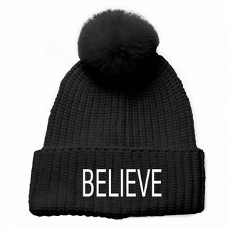 Black knit beanie hat with coordinating faux fur pom pom with embroidered white BELIEVE