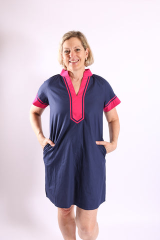 Woman modeling the Candi Color Block Dress in navy with magenta trim, hands in pockets, smiling in a studio setting.