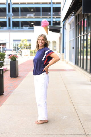 Woman outdoors in navy Ziggy Shirt with red and white wavy trim, styled with white pants for a patriotic look