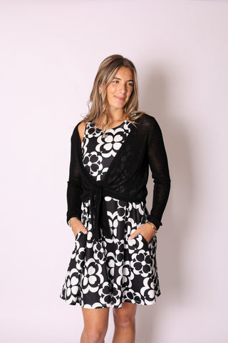 Model wearing the Kara Knit Wrap in black, styled over a black and white floral dress.