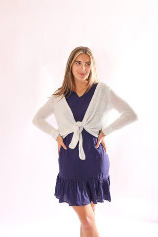 Model wearing the Kara Knit Wrap in silver, layered over a navy ruffle dress.