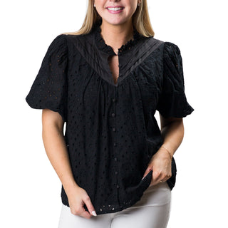  black eyelet top with short puffed sleeves and a ruffled V-neckline. The top features intricate eyelet detailing throughout and fabric-covered buttons down the front. 