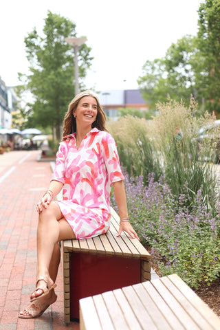 Woman sitting outdoors in the Sage Dress featuring bright pink and coral reef-inspired print, styled for spring outings