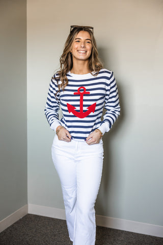 Woman wearing the Scout Sweater with navy and white stripes and a bold red embroidered anchor, paired with white pants.