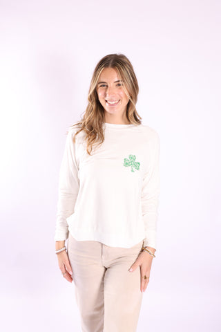Seasonal Stitch Top with green shamrock embroidery, styled with beige pants.