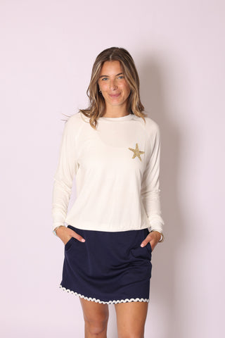 Woman modeling cream Seasonal Stitch Top with gold starfish embroidery, paired with navy skirt.