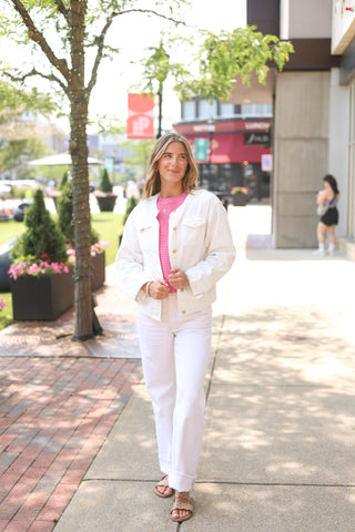 Lifestyle shot of woman walking outdoors in white Coco Jean Jacket, styled with pink top and white jeans.