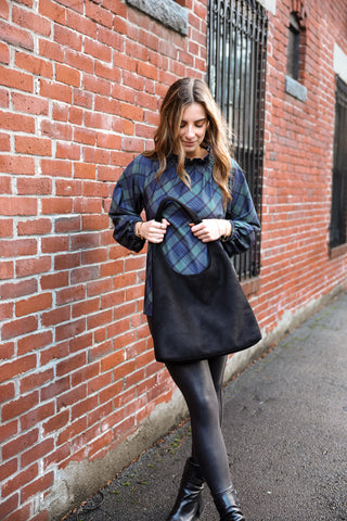 Woman wearing a plaid shirt holding a black hobo bag against a brick wall.