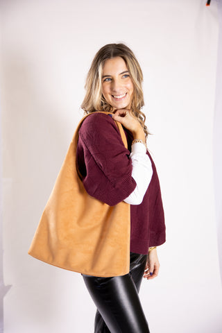 Woman holding a large tan handbag against a plain background