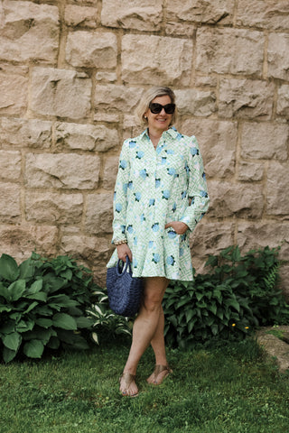Lifestyle image of woman wearing the Dottie Dress in green floral lattice print, styled with blue woven bag and sandals.