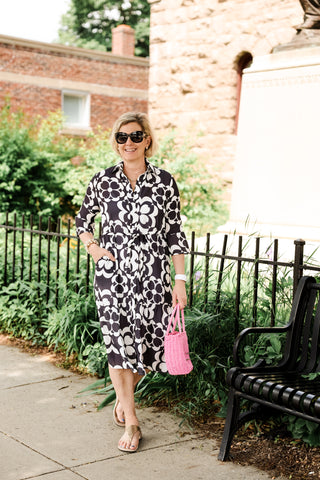 Woman wearing a black and white floral dress carrying the Lani Half Circle Rafia Bag in bright pink with drawstring closure.