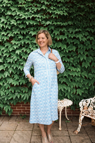 Outdoor lifestyle shot of The Lennon Dress in blue geometric print, styled with neutral shoes and bracelet.