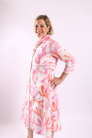 Woman wearing The Lennon Dress in pink and coral abstract print with 3/4 sleeves and embroidered trim, side pose.