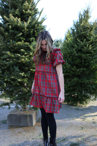 Woman wearing a red plaid dress standing in front of Christmas trees.