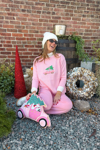 Person in pink outfit with Christmas-themed plush toy sitting on gravel in front of a brick wall.